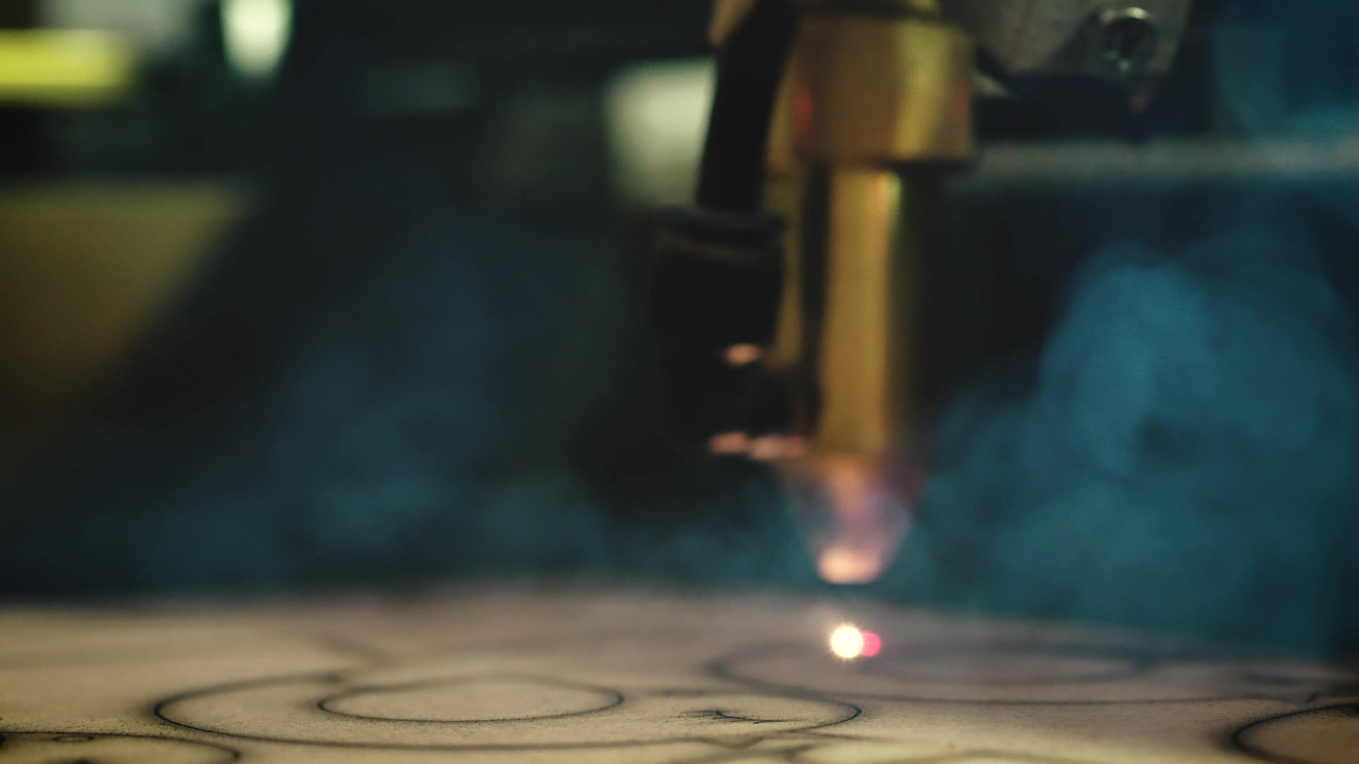 Industrial laser cutting head moving across a workpiece, with a visible beam and smoke